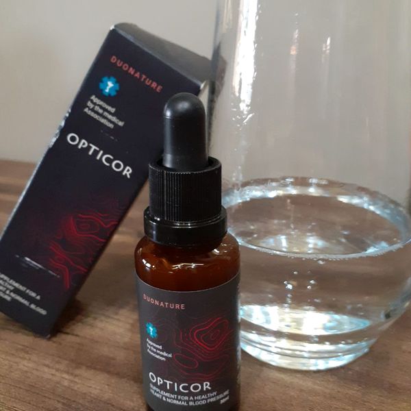 Flacone ambrato di Opticor con contagocce accanto alla scatola e a un bicchiere d'acqua